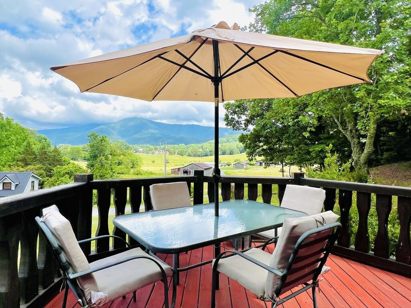 Una terraza con mesa y sillas, un gran paraguas y una vista panorámica de un valle y montañas.