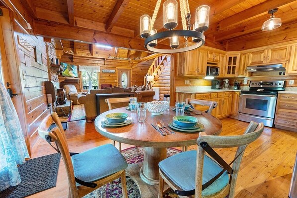 A wooden cabin interior with a dining area, kitchen, and a staircase leading to a loft bedroom.