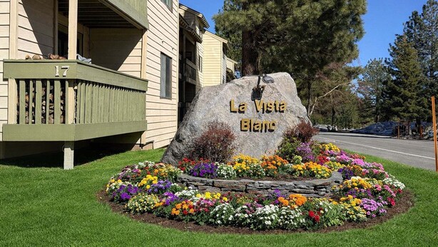 Un edificio con balcón, una gran roca con la inscripción 'La Vista Blanc' y un parterre de flores al frente.