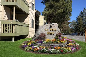 A building with a balcony, a large rock with 'La Vista Blanc' engraved, and a flower bed in front. - La Vista Blanc #16 3 Bedroom Condo by RedAwning (Mammoth Lakes)