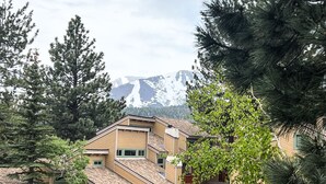 Un edificio de varios pisos con techo inclinado, rodeado de árboles y una montaña al fondo.