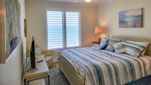 A bedroom with a bed, a desk, a chair, a ceiling fan, and a window with blinds.