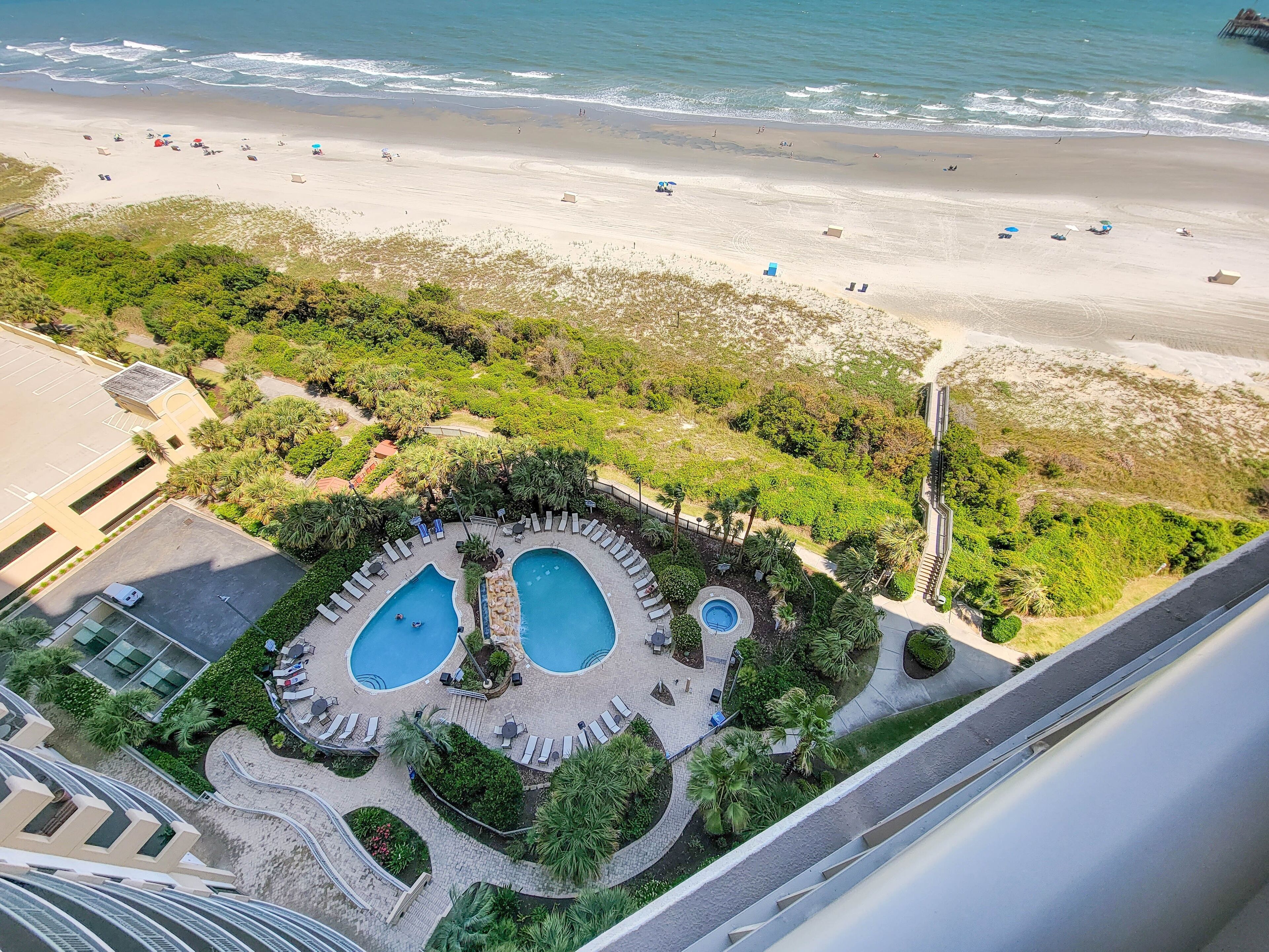A resort with two swimming pools, a beach, and a parking area.
