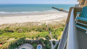 A beach view from a balcony with a pool and lounge chairs.