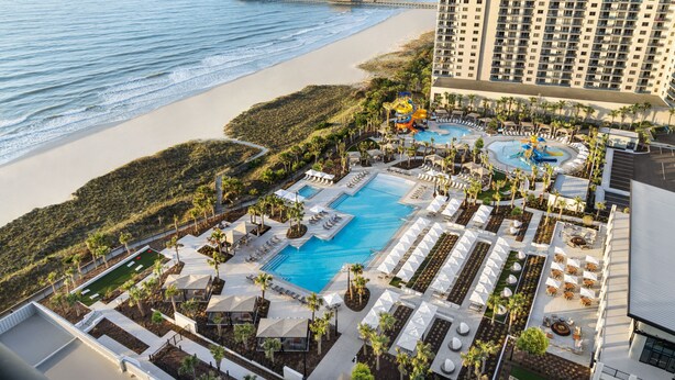 A resort with a large pool, sun loungers, and a beach view.