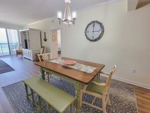 A dining area with a wooden table, green bench, and two chairs. A large wall clock is visible. - 1104 Margate 3 Bedroom Condo (Myrtle Beach)