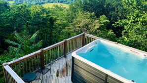 Un jacuzzi en una terraza de madera con vistas a un paisaje verde exuberante y montañas a lo lejos.