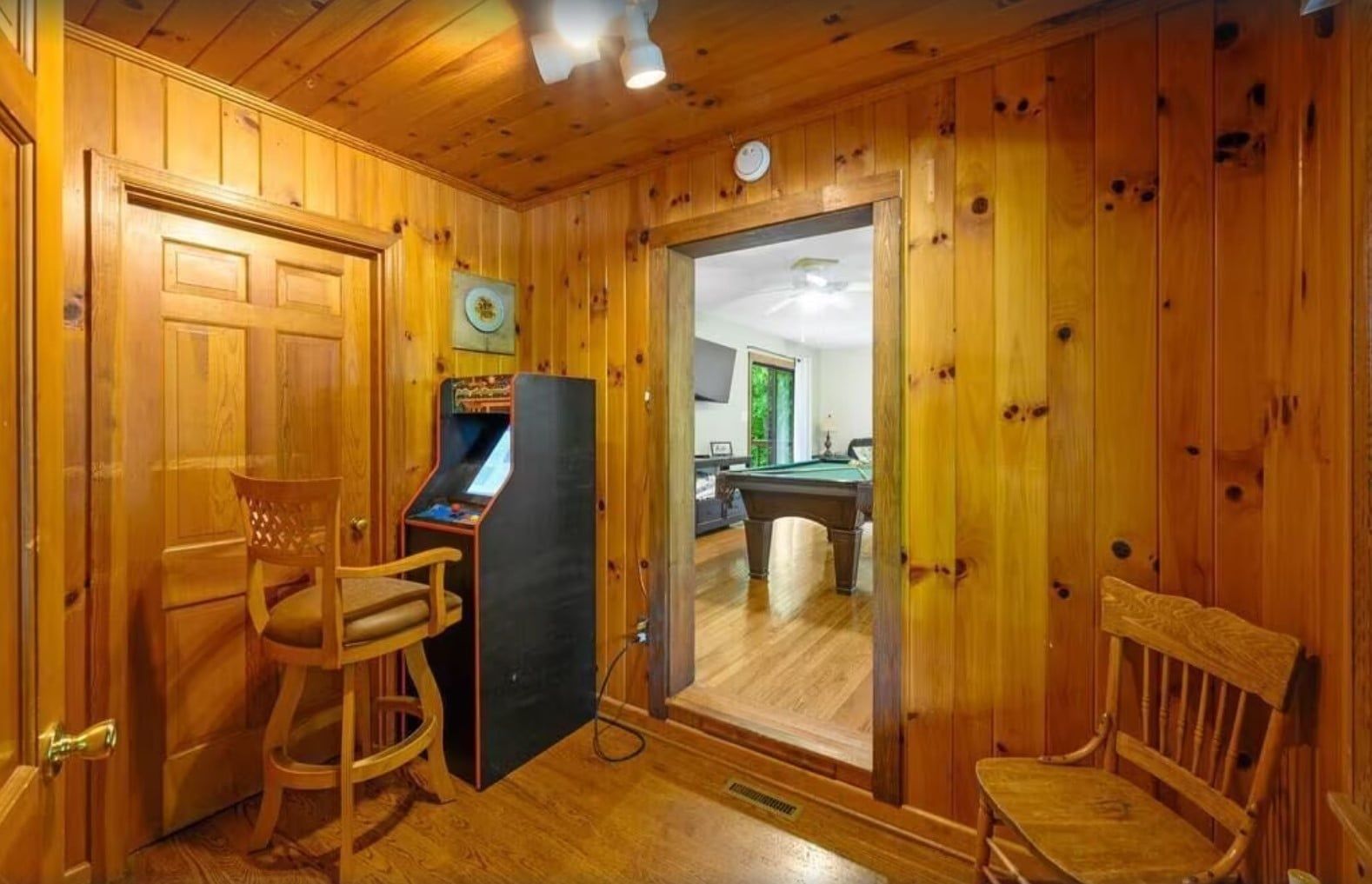 A wooden-paneled room with a pool table, a pool cue, and a pool table chair.