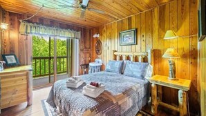 Dormitorio de cabaña de madera con cama, mesita de noche, lámpara y vista a la vegetación.