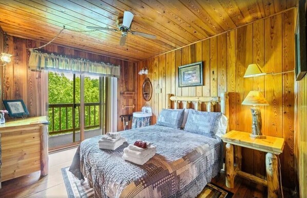 A wooden cabin bedroom with a bed, bedside table, lamp, and a view of greenery outside. - Little Greenbriar Lodge 13 Bedroom Cabin by RedAwning (Sevierville)