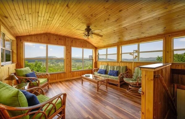 A wooden-paneled room with large windows, wicker furniture, and a ceiling fan. - Little Greenbriar Lodge 13 Bedroom Cabin by RedAwning (Sevierville)