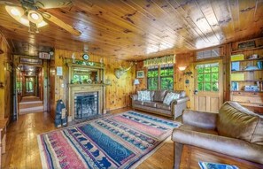 A log cabin interior with a fireplace, leather sofa, and a large rug. - Little Greenbriar Lodge 13 Bedroom Cabin by RedAwning (Sevierville)