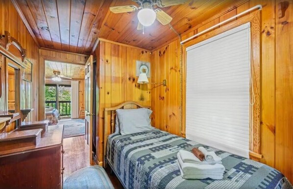 A wooden cabin bedroom with a bed, a desk, and a window.