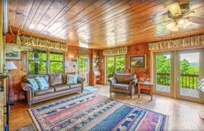 A cabin interior with a wooden ceiling, a large rug, a sofa, a chair, and a view through the door. - Little Greenbriar Lodge 13 Bedroom Cabin by RedAwning (Sevierville)