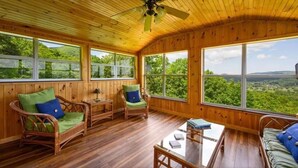 Una habitación con paneles de madera, muebles de mimbre, ventanas grandes y un ventilador de techo.