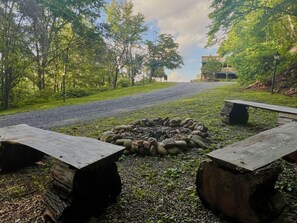 A campsite with a fire pit surrounded by stones, two benches, and a gravel path leading to a building. - Little Greenbriar Lodge 13 Bedroom Cabin by RedAwning (Sevierville)
