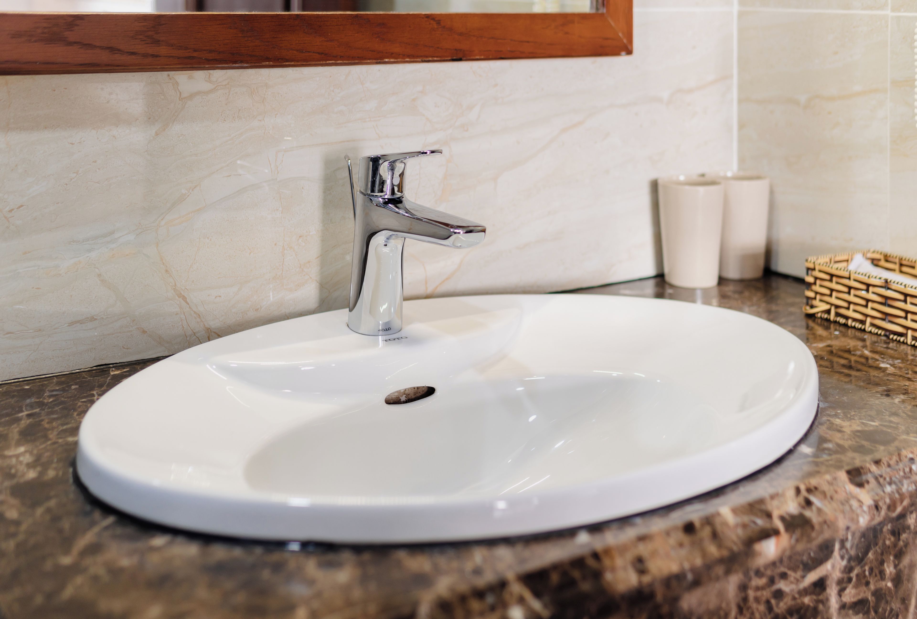 A white bathroom sink with a chrome faucet, a marble countertop, and a wooden-framed mirror above it.