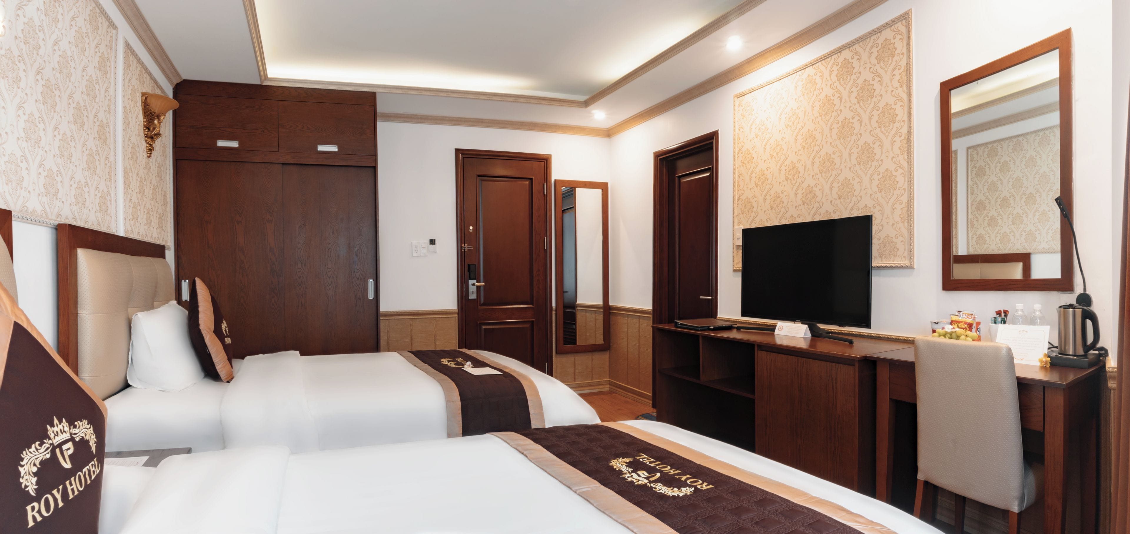 A hotel room with two beds, a television, a desk with a coffee maker, and a mirror.