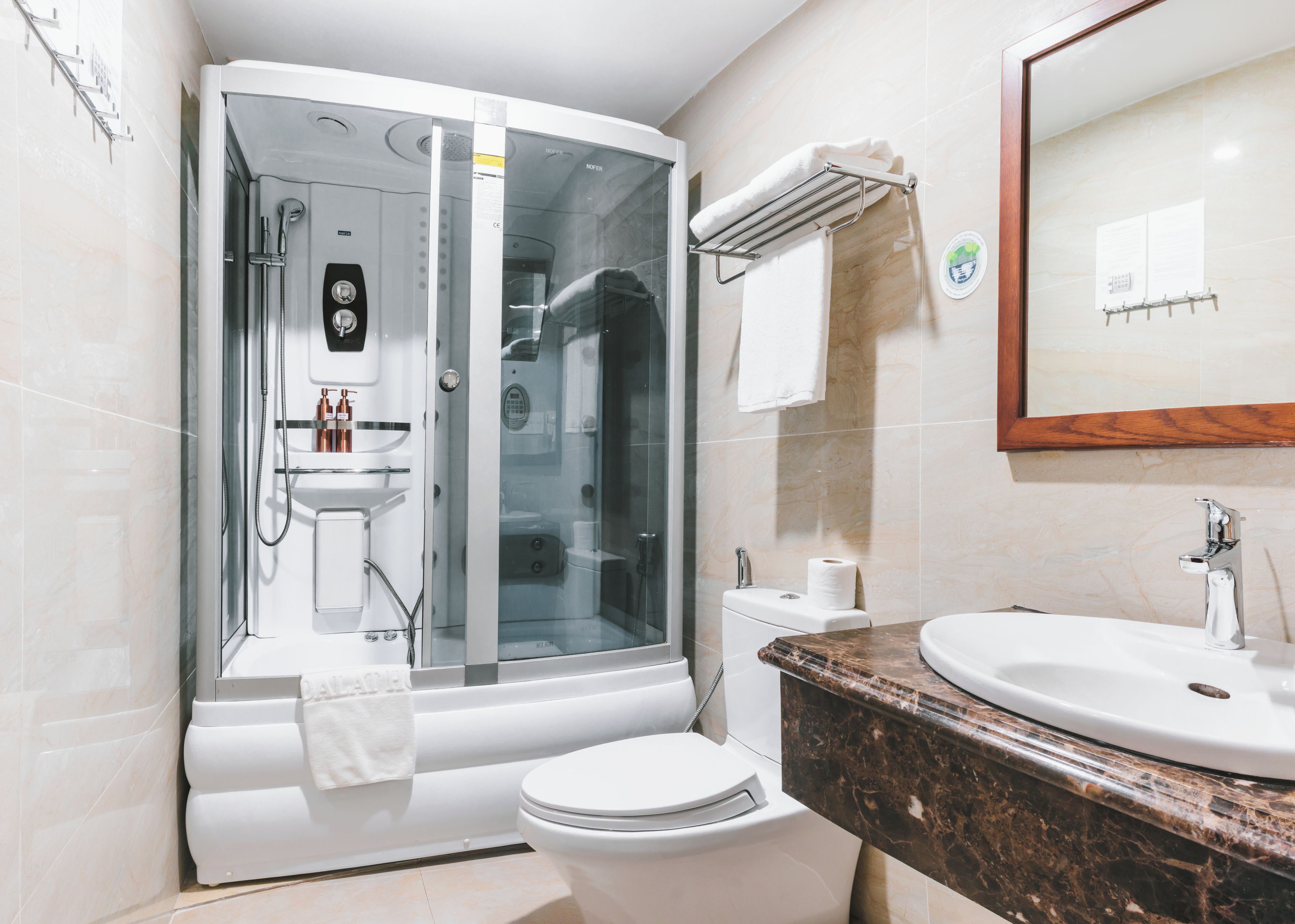 Un baño moderno con ducha envuelta en vidrio, inodoro blanco, lavamanos con encimera de mármol y espejo con marco de madera.