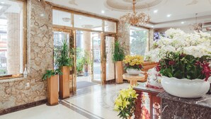 Un hall de hotel con paredes de mármol, una araña, plantas en macetas y una recepción.