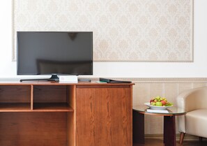 A modern living room with a flat-screen TV on a wooden stand, a small side table with a fruit bowl, and a beige sofa. - ROY Dala Hotel (Xuan Huong - Da Lat)