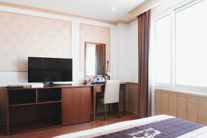 Een hotelkamer met een bed, een bureau met een televisie, een spiegel en een raam met gordijnen.