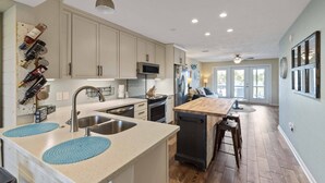 A modern kitchen with stainless steel appliances, a wooden island, and a backsplash with wine bottles. - Narvana-Gulf View Home Across from Beach. Pup Friendly (Navarre)