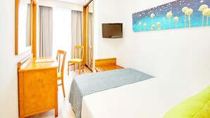 A hotel room with a bed, a desk, a chair, a television, and a painting on the wall. - Universal Hotel Laguna (Capdepera)
