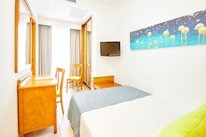 Quarto de hotel com cama, escrivaninha, cadeira, televisão e um quadro na parede.