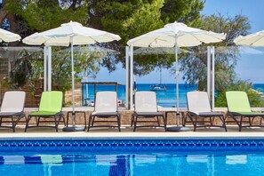 A poolside area with lounge chairs and umbrellas, a clear view of the sea, and a wooden deck.