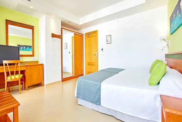Quarto com cama, escrivaninha e cadeira. Uma porta dá acesso a outro cômodo.