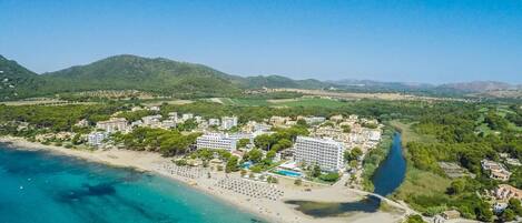 An aerial view of a coastal resort with a beach, hotel buildings, and a river.