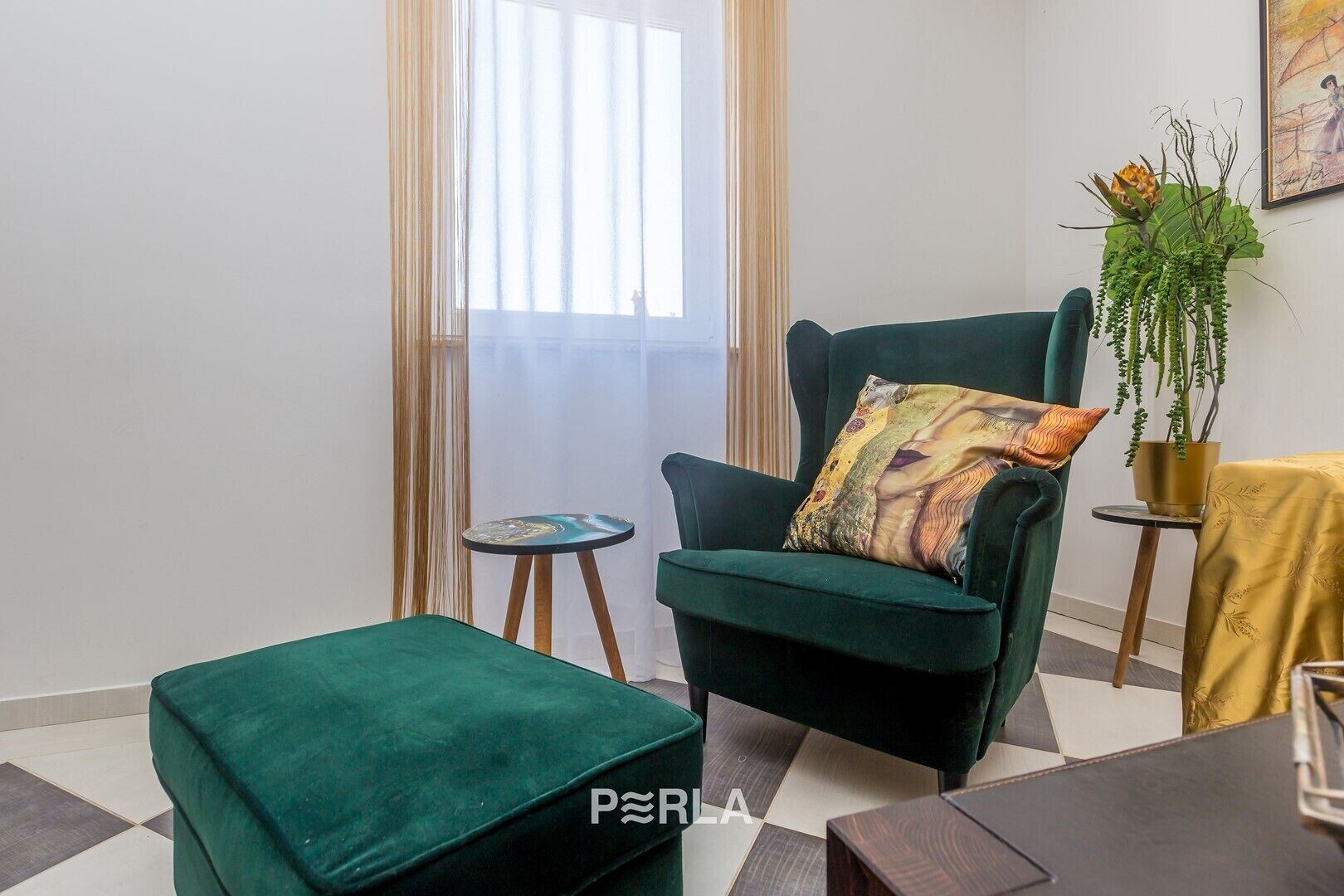A living room with a green armchair, a matching ottoman, a small round table, and a potted plant.