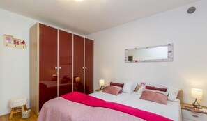 Ein Schlafzimmer mit einem Bett, Nachttischen, einem Kleiderschrank, einem Spiegel und einem kleinen Hocker.
