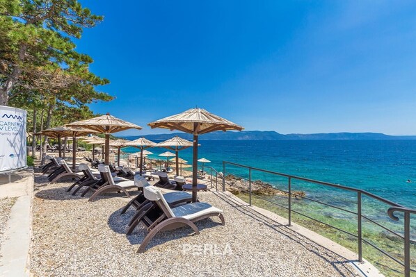 A seaside resort with sun loungers, umbrellas, and a clear view of the ocean.
