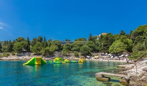 A beach with clear blue water, inflatable play structures, and a rocky shoreline.