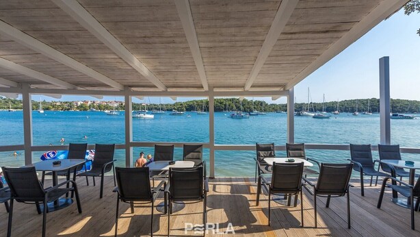 A covered outdoor seating area with tables and chairs, overlooking a marina with boats. - Apartment OLIVE with private garden 250m2 (Vinkuran)