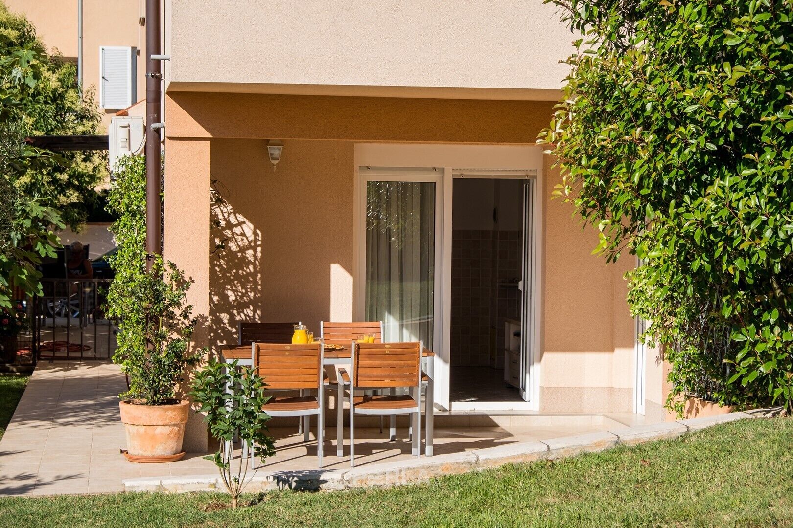 A patio with a table and chairs, a potted plant, and a sliding glass door leading to an interior space.