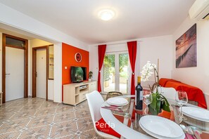 Ein Essbereich mit Tisch für vier Personen, einem Fernseher auf einem Schrank und einem Farbkonzept in Rot und Weiß.