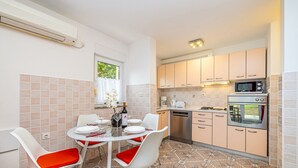 A compact kitchen with a dining area, featuring a round table with chairs, a built-in oven, microwave, and a dishwasher. - Apartment OLIVE with private garden 250m2 (Vinkuran)