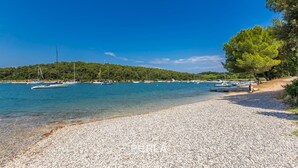 A pebble beach with boats and a forested hill in the background. - Apartment OLIVE with private garden 250m2 (Vinkuran)