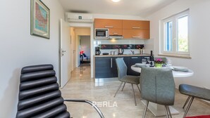 A modern kitchen with a central island, a dining area with a round table and chairs, and a visible air conditioning unit.