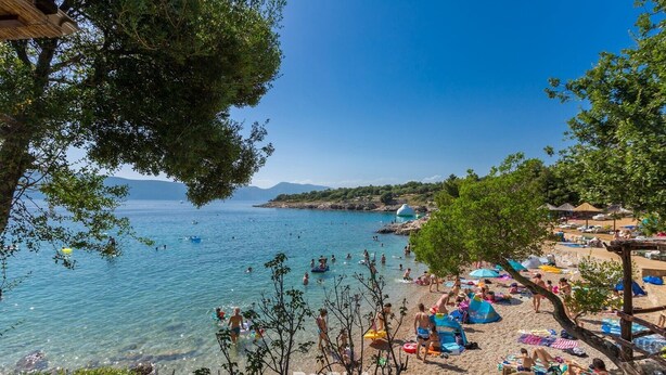 A beach with clear waters, umbrellas, and people enjoying the sun.