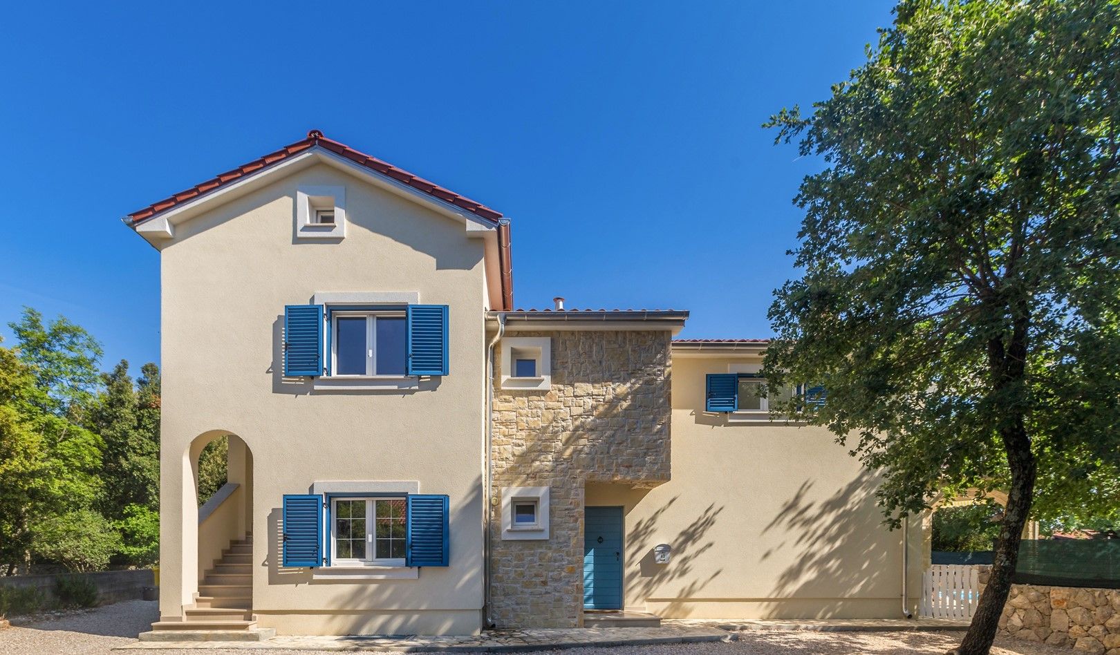 A two-story house with a stone facade, blue shutters, and a red roof.