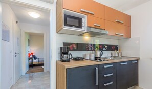 A modern kitchen with a microwave, coffee maker, and kettle. There is a sink and a countertop with cabinets.