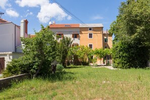 Un immeuble résidentiel doté d’un toit recouvert de tuiles, de nombreuses fenêtres et d’un jardin agrémenté d’arbres et de pelouse.