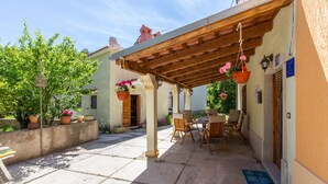 Ein überdachter Außenbereich mit einer Pergola, Blumentöpfen und einem Tisch mit Stühlen.