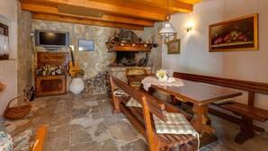 Ein rustikaler Innenraum mit Kamin aus Stein, Holzbalken, einem Fernseher und einer Gitarre.