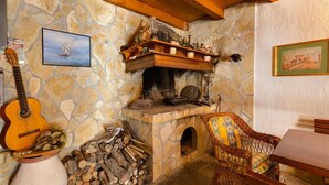 Ein rustikaler Kamin aus Stein mit Holzmantel, eine Gitarre, ein Korbstuhl und ein Tisch in einem gemütlichen Raum.