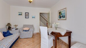 Ein Wohnzimmer mit einem gemusterten Sofa, einem kleinen Tisch mit Blumenvase und einer Treppe, die zu einem anderen Raum führt.